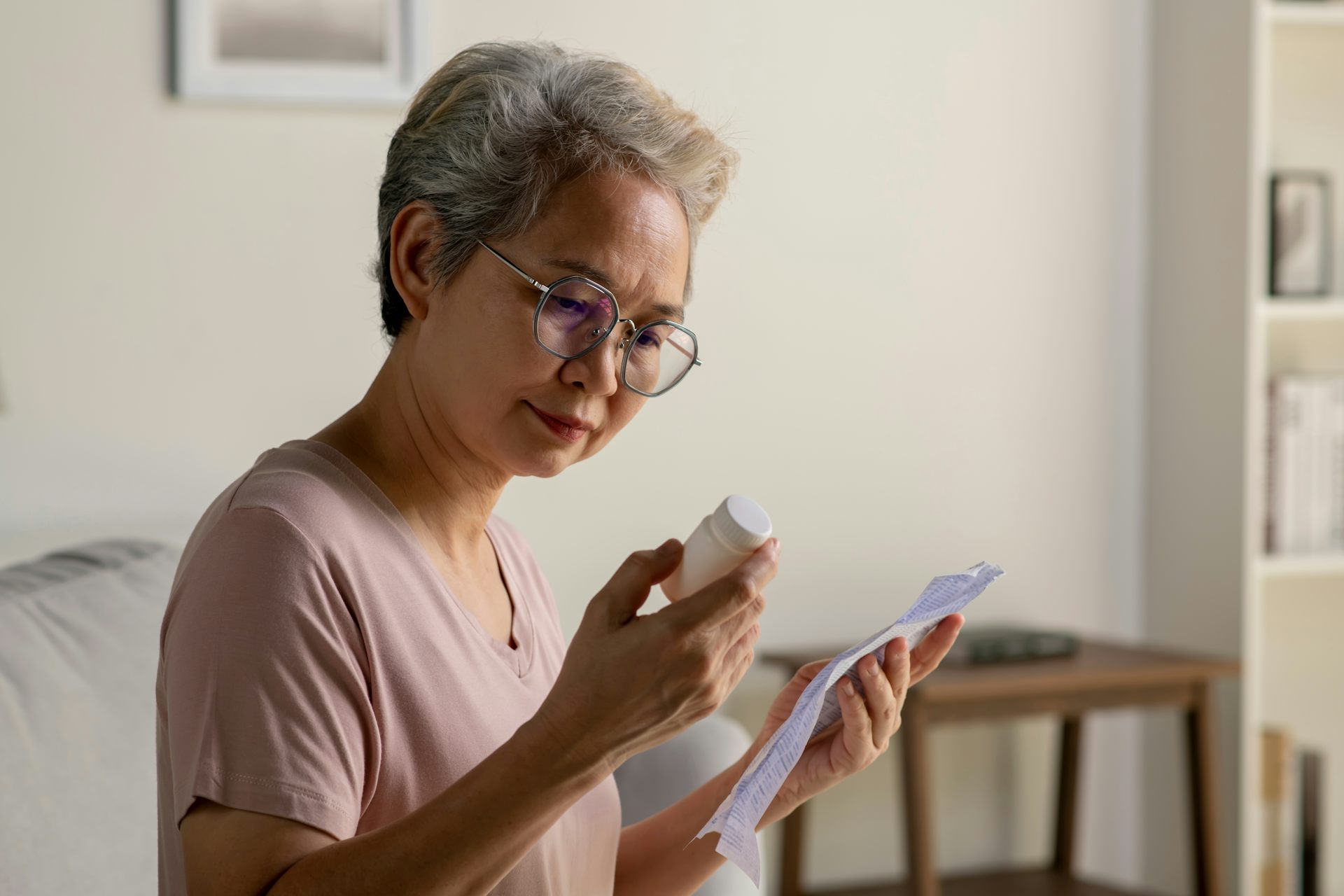 An older woman reviews the medicine leaflet while holding the bottle of medicine.