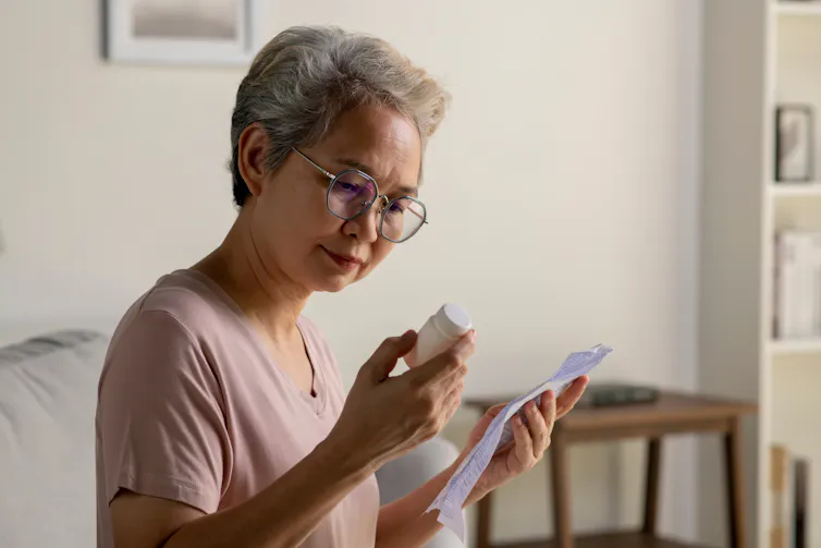 An older woman reviews the medicine leaflet while holding the bottle of medicine.