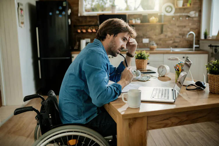 Un jeune homme en fauteuil roulant est assis devant son ordinateur