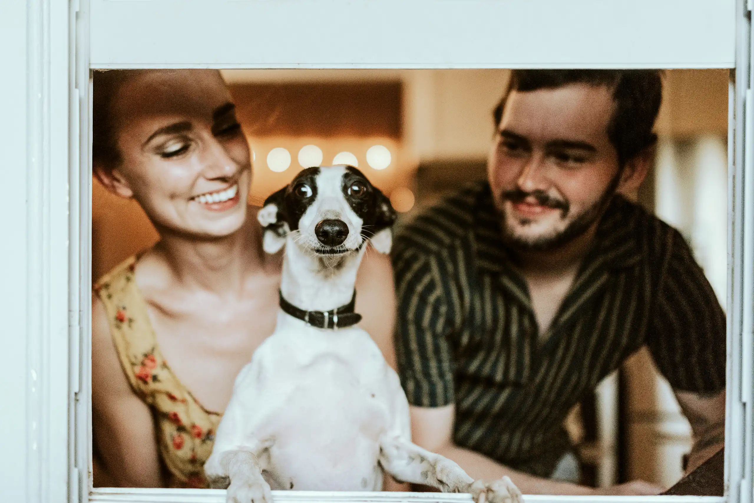 Portrait d'une jeune femme et d'un homme avec leur chien, posant à la fenêtre.