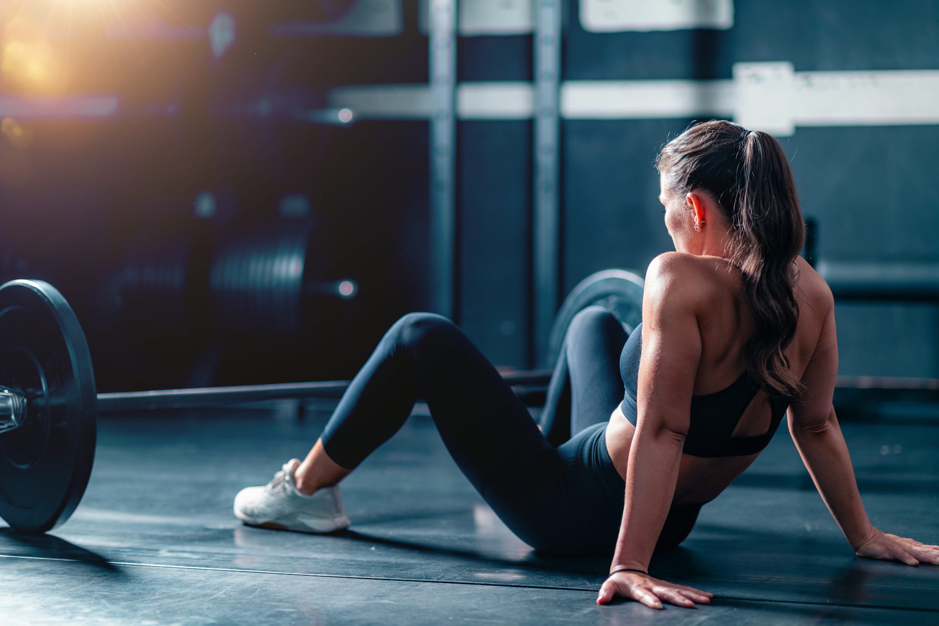 A woman rests on the floor behind a barbell.