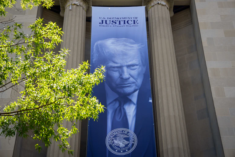 A huge banner with the image of President Trump hangs on a large, columned building.