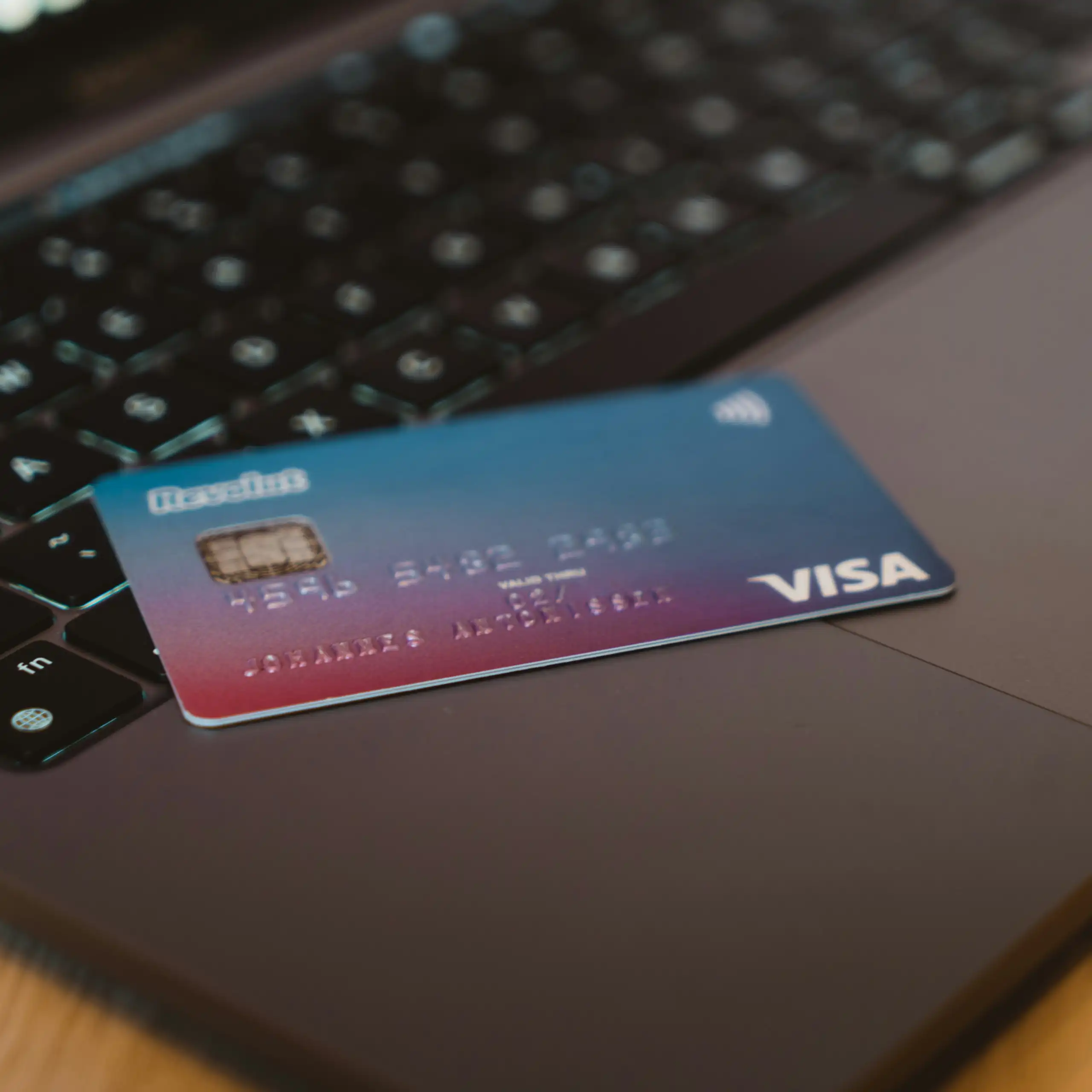 A blue Visa credit card rests on a grey laptop.