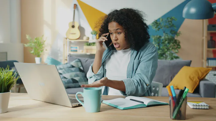 An upset young woman talks on the phone to dispute something she sees on her computer screen.