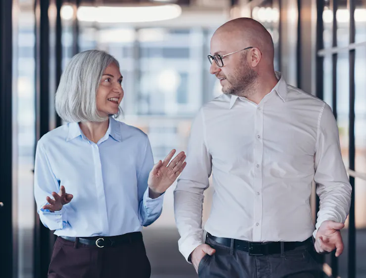 Woman and man walk toward camera, both wearing tucked-in, button-down shirts