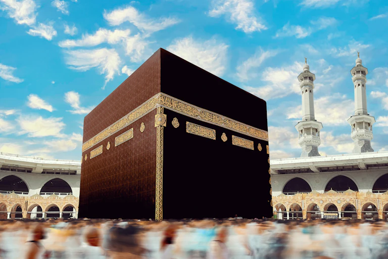 A large cube-like structure covered with a black cloth with minarets in the background.
