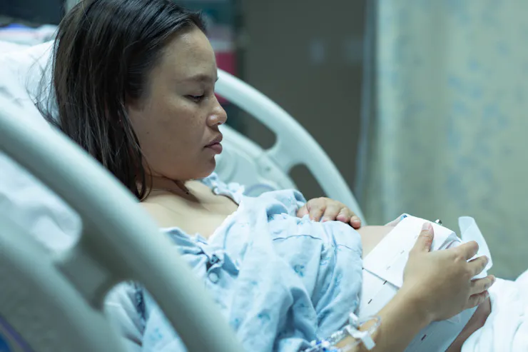 A woman lies in a hospital bed, touching her stomach.