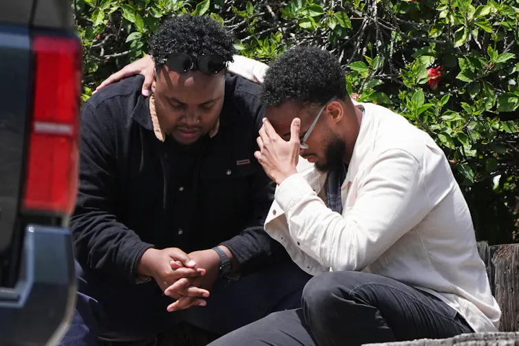 Two men are sitting on the floor and mourning together outside of a building.