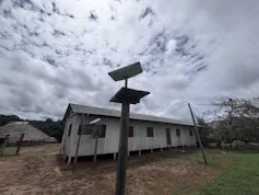 Foto mostra aldeia, com casa de madeira. Em primeiro plano, um poste com uma antena da Starlink