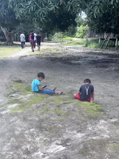 Foto mostra duas crianças indígnenas sentadas na grama, mexendo cada uma com um celular.