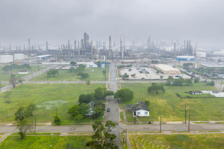 Why Corpus Christi faces a looming water scarcity, and what may assist 1 A neighborhood with grassy lawns and trees is in the foreground, with a massive industrial complex in the background.