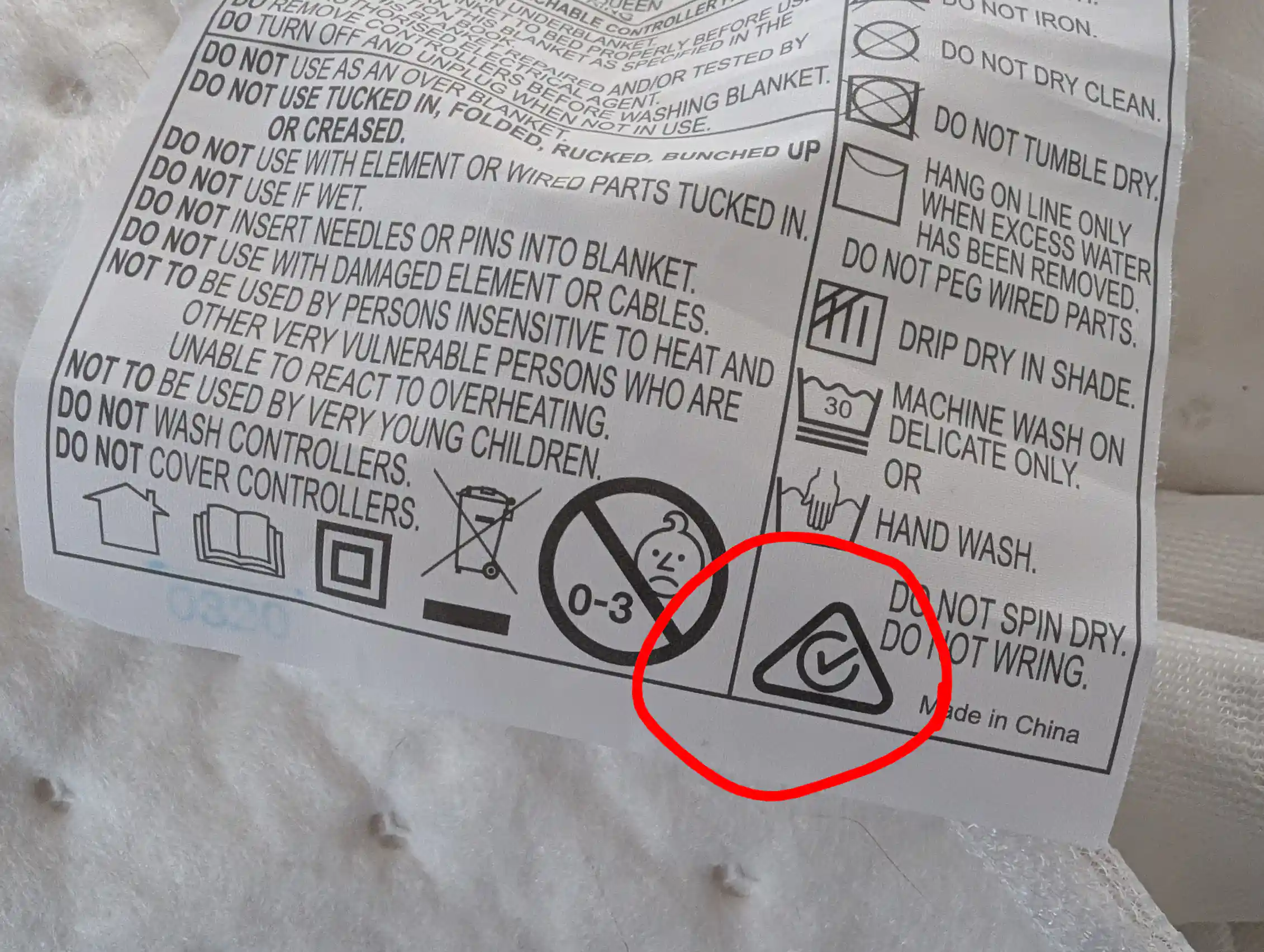 A blanket tag with safety instructions and a tickmark in a triangle circled in red.