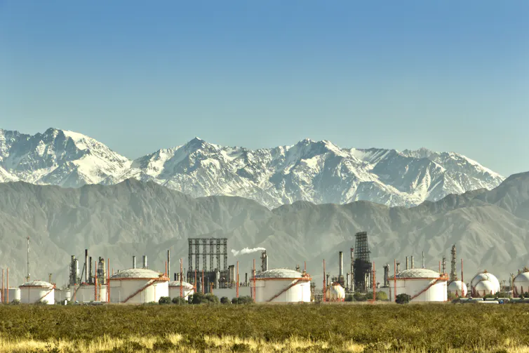 oil refinery in foreground, large snowy mountains behind.