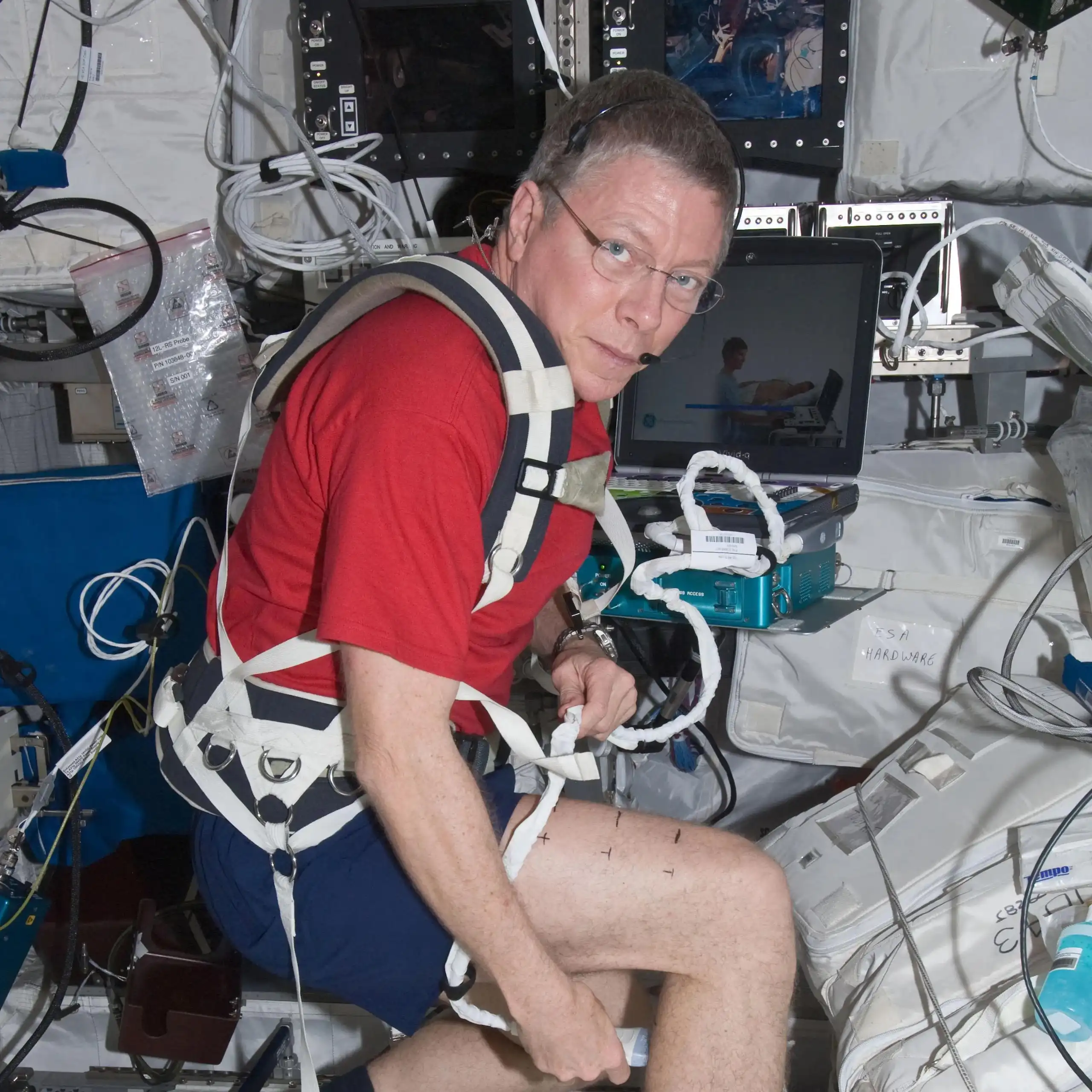 A man in a red t-shirt wears a harness and holds medical equipment.