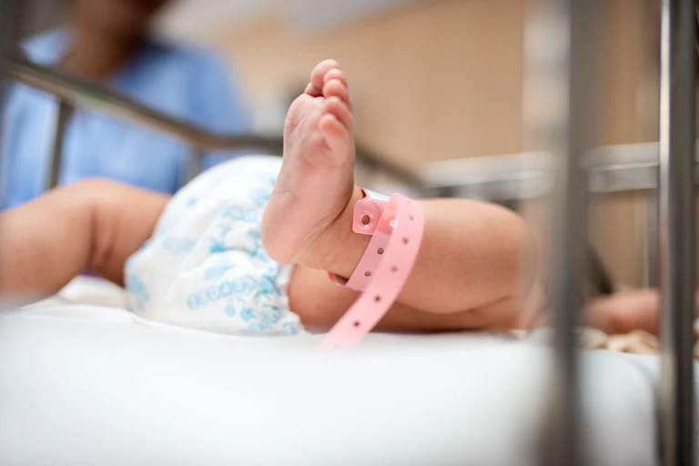 Gros plan sur les pieds d'un nouveau-né avec un bracelet rose d'hôpital, qui est couché dans un berceau.