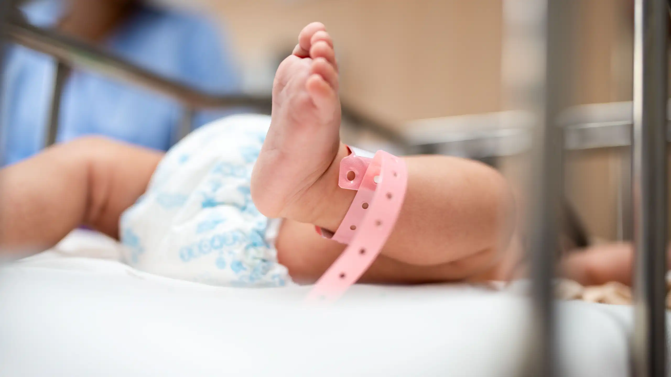 Gros plan sur les pieds d'un nouveau-né avec un bracelet rose d'hôpital, qui est couché dans un berceau.