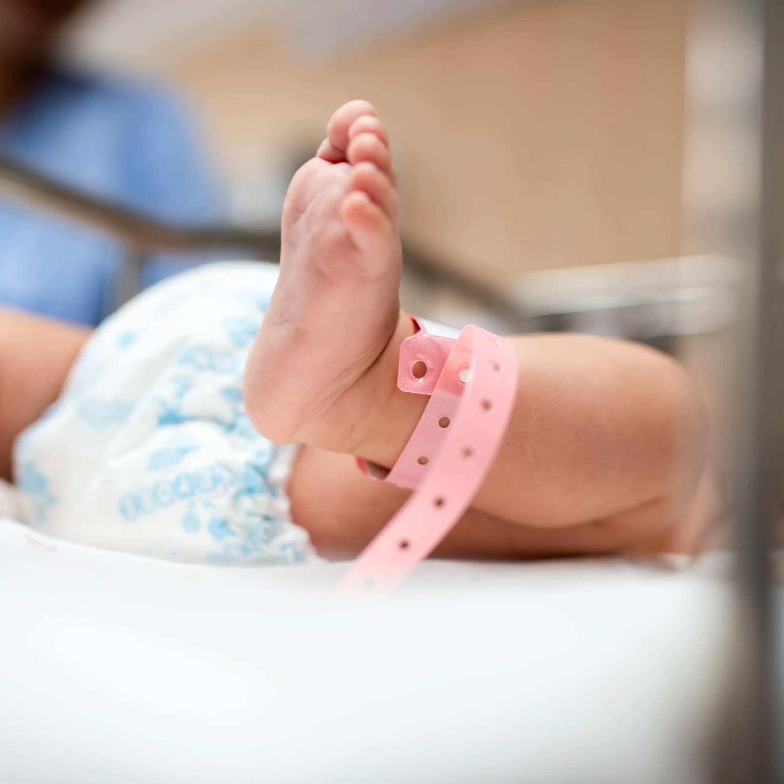 Gros plan sur les pieds d'un nouveau-né avec un bracelet rose d'hôpital, qui est couché dans un berceau.