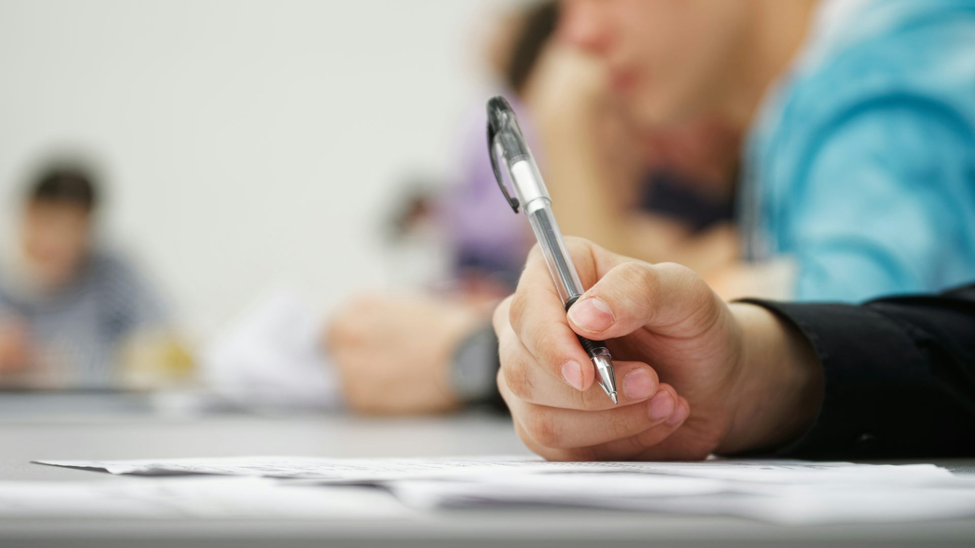Una mà sosté un bolígraf en una taula davant d'uns papers.