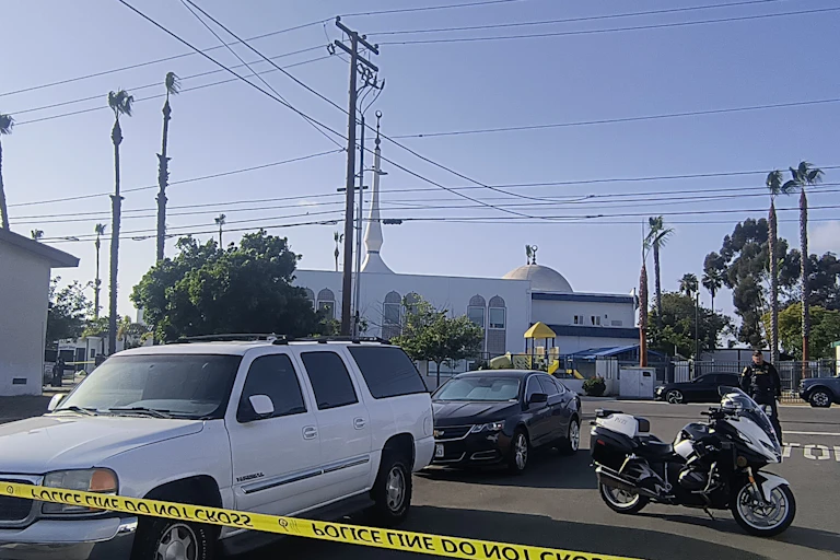 A white mosque in the background, cars in a car park and a police cordon in the foreground
