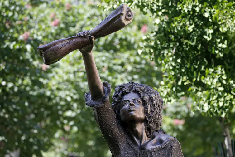 A statue despite a woman holding a piece of paper in defiance.