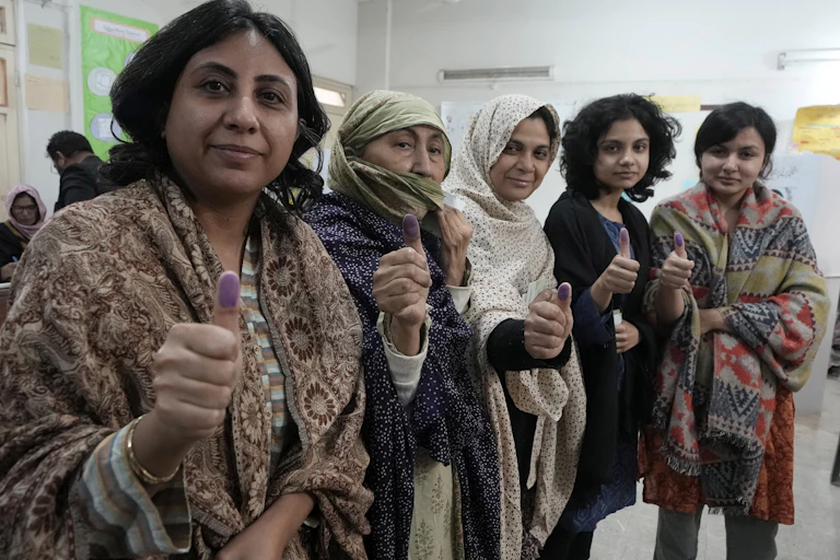 Women hold up their thumbs at a voting station.