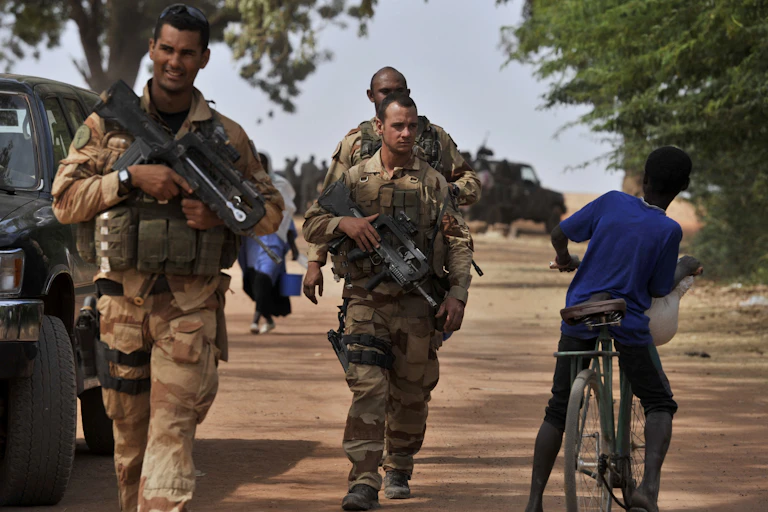 Armed men in military uniform walk past a cyclist