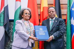 A woman and man smiling at a camera while holding a large blue book between them.