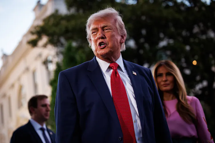 Portrait of Donald Trump with Melania in the background.
