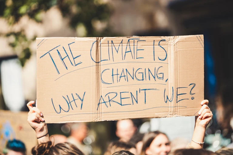 protestors hold cardboard placard with handwritten message: the climate is changing why aren't we