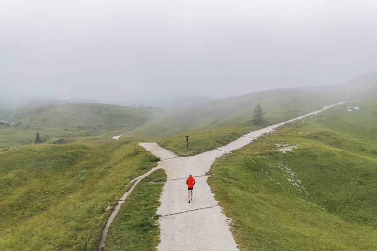 A runner approaches a fork in the road, with a small path off to one side.