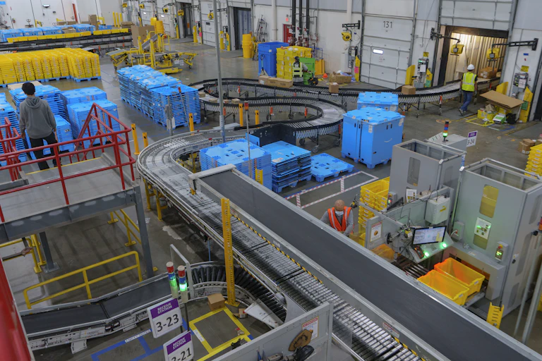 Amazon workers unload blue pallets of goods off of truck trailers at a fulfillment center in Oxnard, Calif.