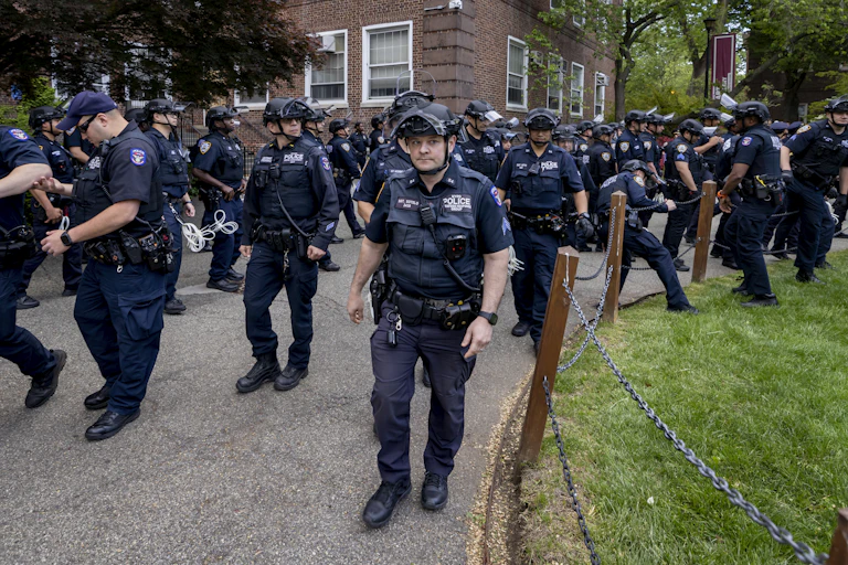 Dozens of police officers walk in unison through a college campus.