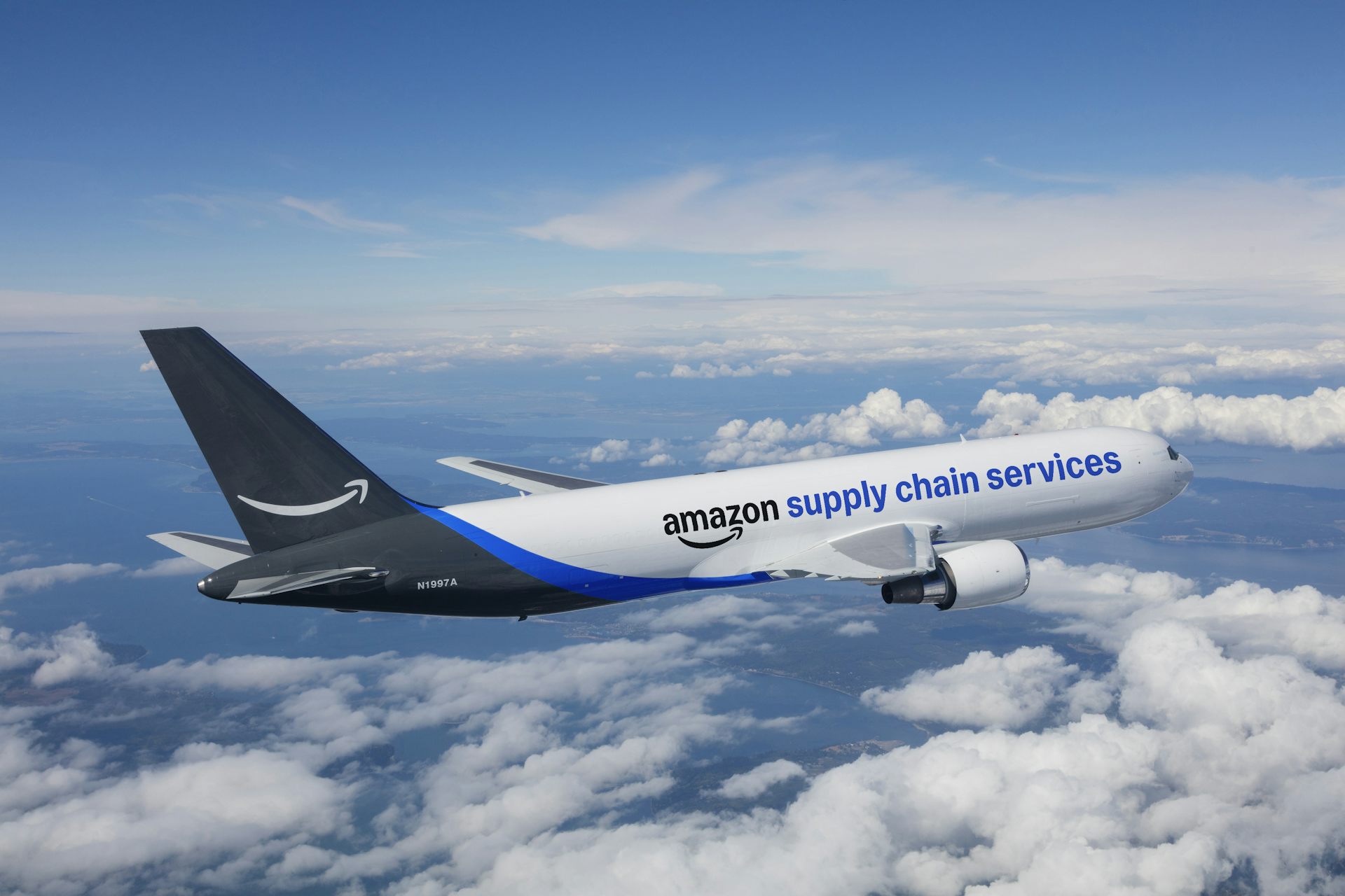 A blue and white airplane labeled Amazon Supply Chain Services flies over clouds.