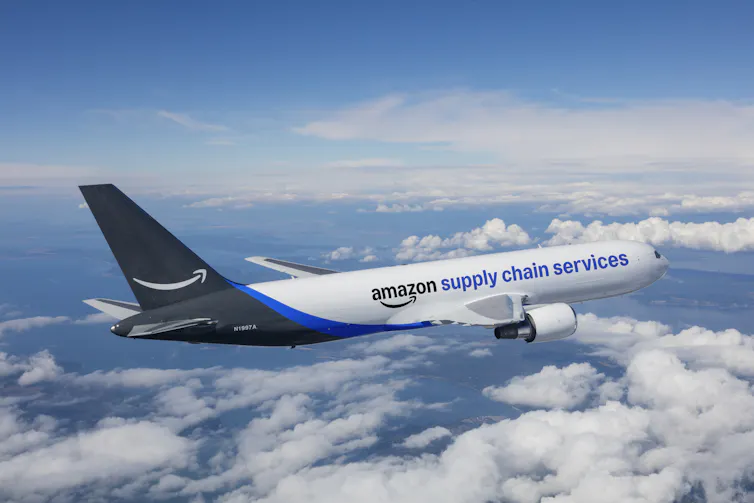 A blue and white airplane labeled Amazon Supply Chain Services flies over clouds.