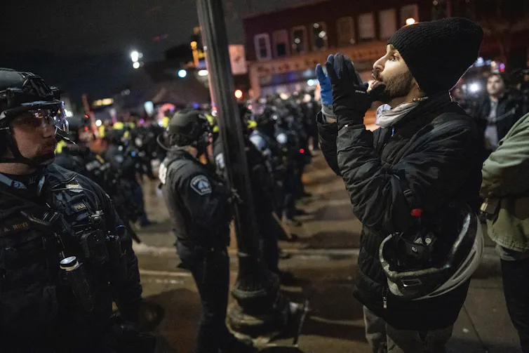 A man dressed in black faces dozens of police officers.