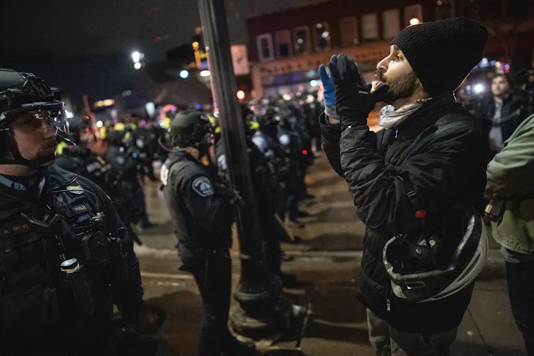 A man dressed in black faces dozens of police officers.