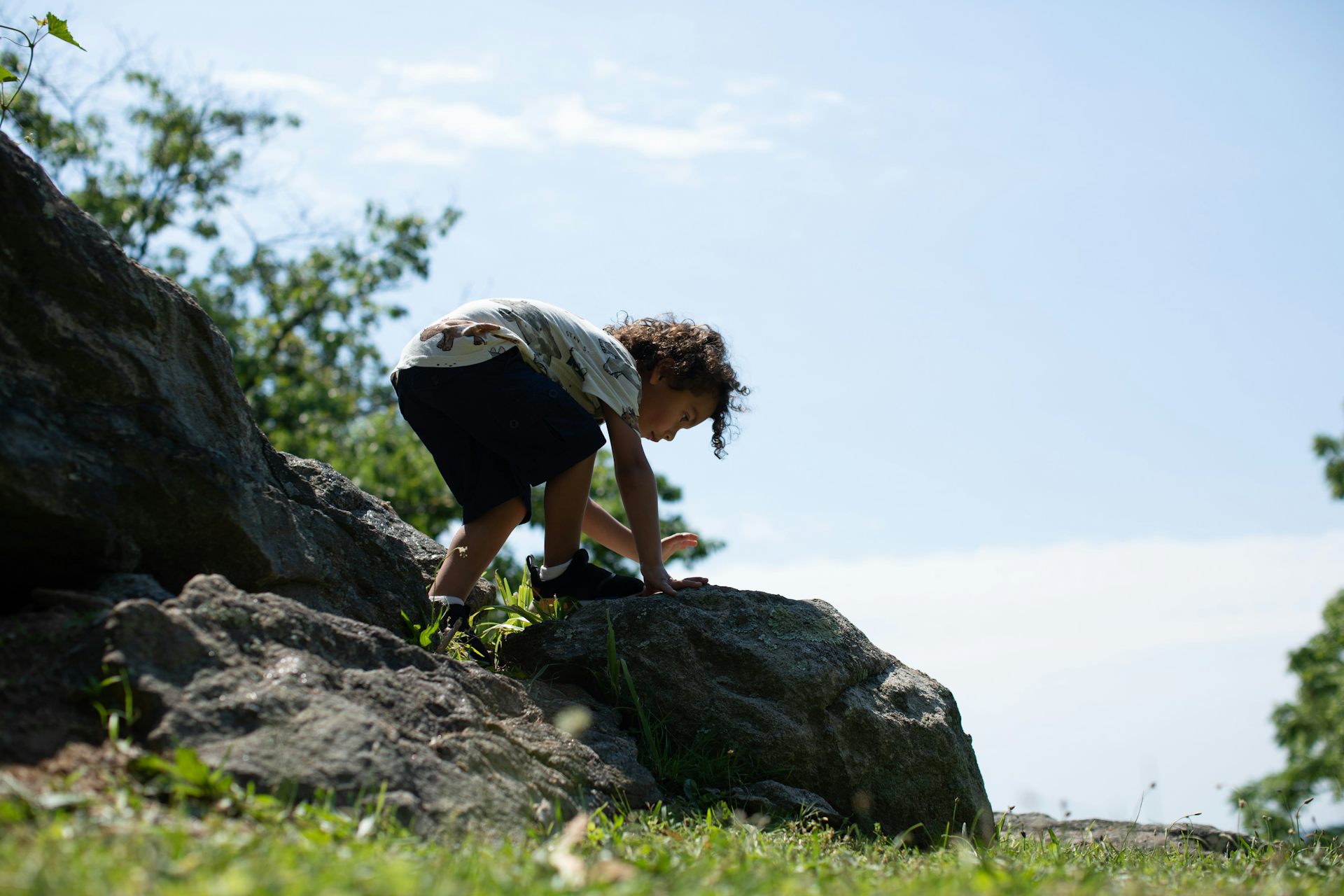 Un niño pequeño sube a las rocas junto a la hierba.
