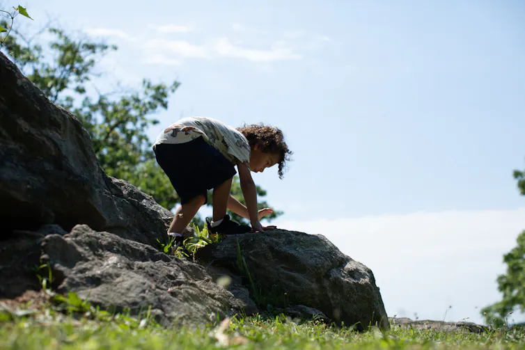 A young child scrambles atop boulders next to grass.