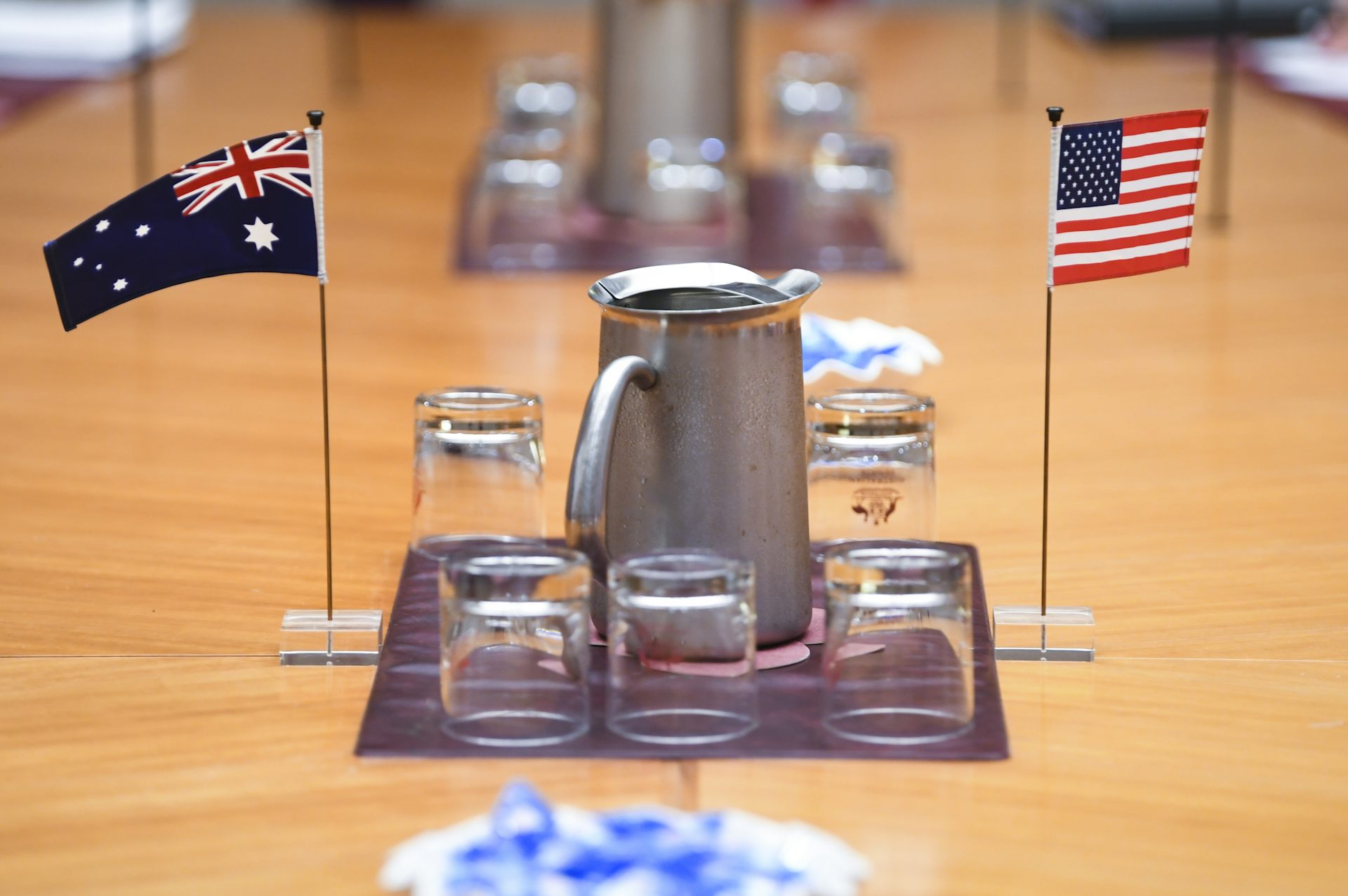 Small Australian and US flags are seen on a table near some glasses and jugs of water