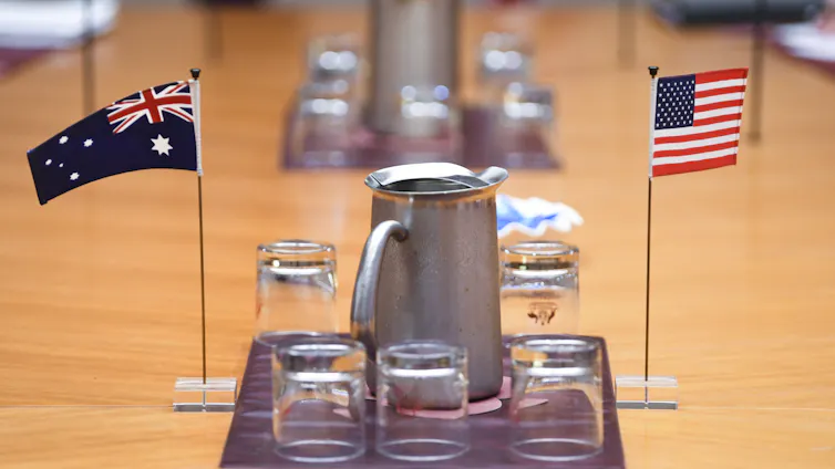 Small Australian and US flags are seen on a table near some glasses and jugs of water