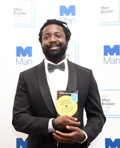 a Black man in a tuxedo holding his book