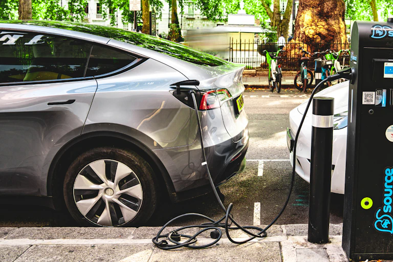 Two cars are parked on a leafy street and plugged into a kerbside charger.