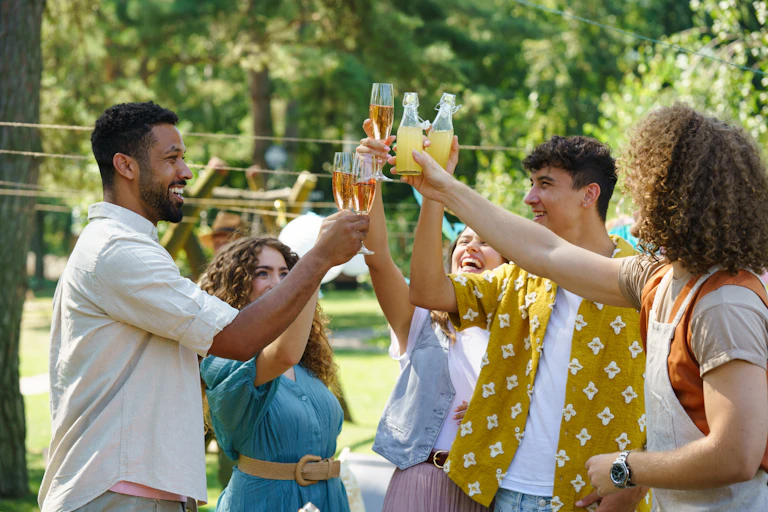 A group of young adult friends cheers their glasses. Some glasses are filled with beer, while others are filled with juice.