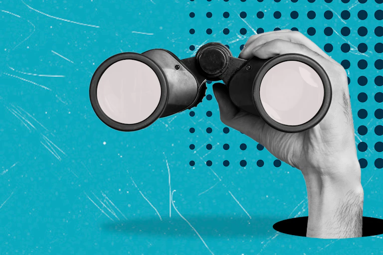 Hand holding pair of binoculars on blue background.