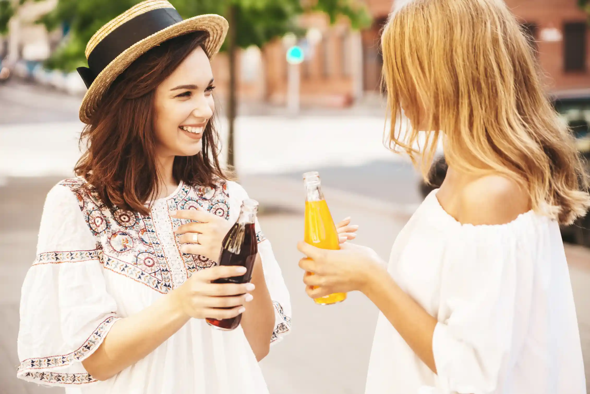 Dos jóvenes se sonríen mutuamente; una sostiene una botella de Coca-Cola o Pepsi y la otra una botella de Fanta o zumo de naranja.
