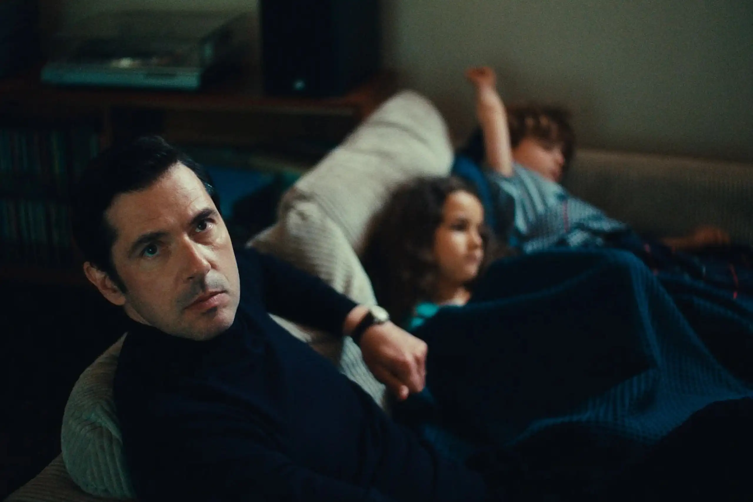 Image tirée du film, Melvil Poupaud sur un canapé regardant la caméra, les deux enfants du personnage qu'il joue sont à côté de lui.