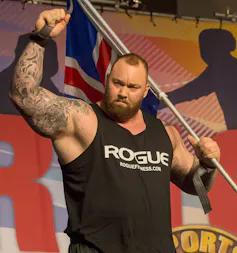 A large man in a weightlifting competition raises his arm as a show of strength.