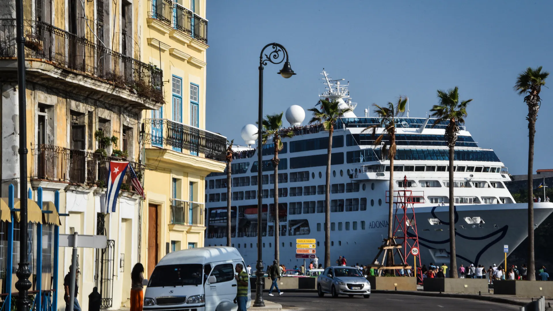 A cruise ship lands very close to buildings that are very old, with palm trees nearby.