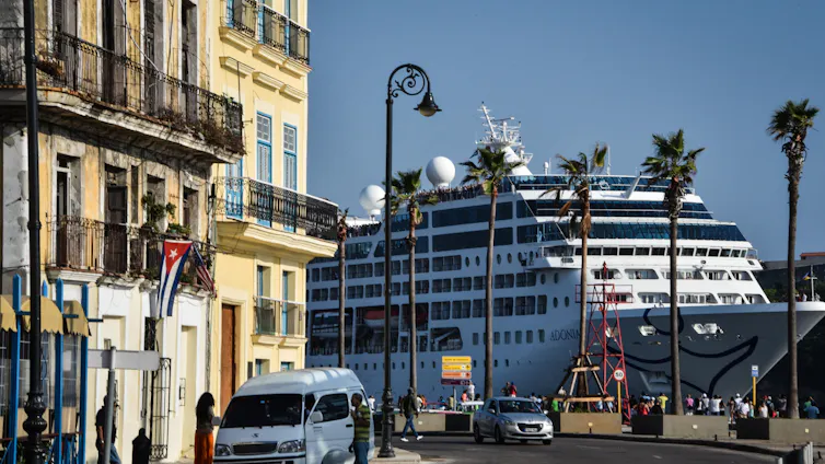 A cruise ship lands very close to buildings that are very old, with palm trees nearby.