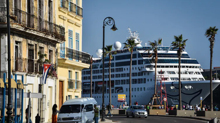 A cruise ship lands very close to buildings that are very old, with palm trees nearby.